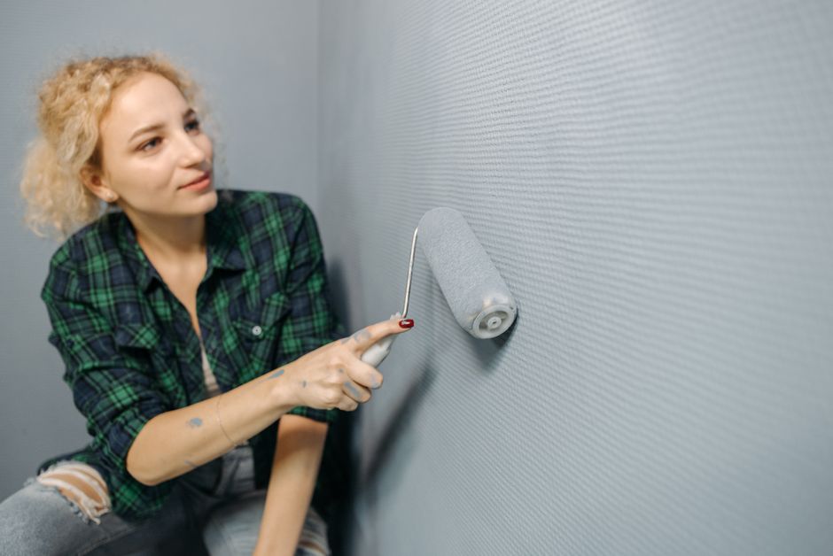 A woman uses a paint roller to apply paint on a wall, part of a home renovation project.